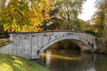 Cambridge, England. View of King's College Bridge over the River Cam with several students walking across, framed by water, college grounds, and surrounding greenery