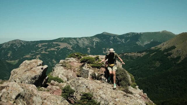 A woman climbs rocky terrain on Babin Zub mountain in Serbia Stara Planina National Park, surrounded by dramatic landscapes and mountain ridges. Hiking and travel with pets concept
