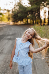 Obraz premium Beautiful nine-year-old blonde girl with long hair in a blue suit, walking in nature in the forest. Summer, sunset