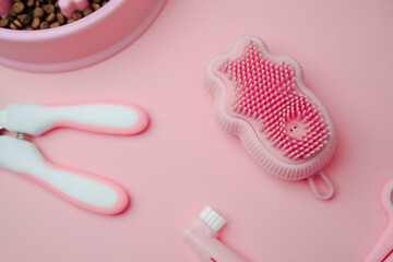 Pet grooming tools, nail clippers, brush, and food bowl with kibble on a pink surface.