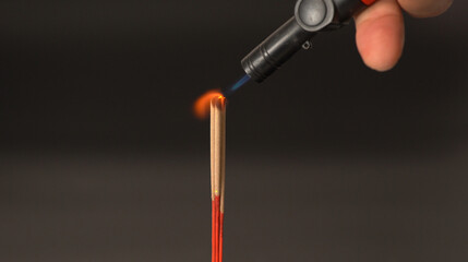 Lighting incense stick with small torch flame close up hand holding torch red incense dark background spiritual calm ritual meditation relaxation focus