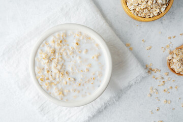 Oatmeal porridge with raw oats and wooden spoon on light background