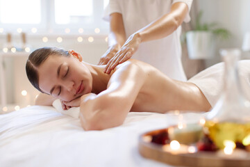 Calm woman enjoying full body massage at spa salon, professional masseur rubbing her shoulders and back in warm candles atmosphere