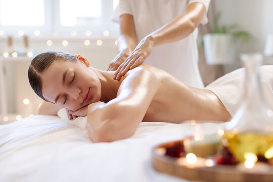 Calm woman enjoying full body massage at spa salon, professional masseur rubbing her shoulders and back in warm candles atmosphere - Powered by Adobe