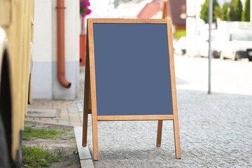 Blank wooden street board with empty blue surface. Outdoor advertising stand on cobblestone sidewalk near building. Urban marketing mockup for restaurant or shop promotion. Street signboard template.