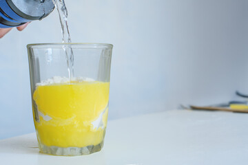 Dissolving protein banana powder in glass of water, closeup photo. Yellow protein shake being mixed with water in glass, fitness nutrition concept