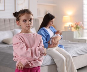 Fototapeta premium Jealous little girl upset about mom spending time with newborn baby at home, selective focus