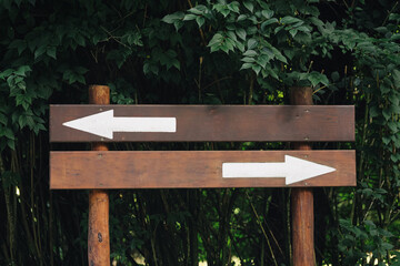 Wooden signpost with two opposite arrows. Blank direction board in natural park environment. Empty guidepost template for navigation and travel. Rustic wooden information sign in forest background. © Paweł Michałowski