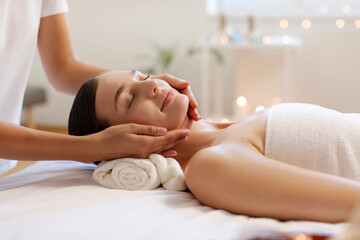 Young woman receiving relaxing face massage at serene atmosphere in spa salon, masseur touching female's chin and cheeks