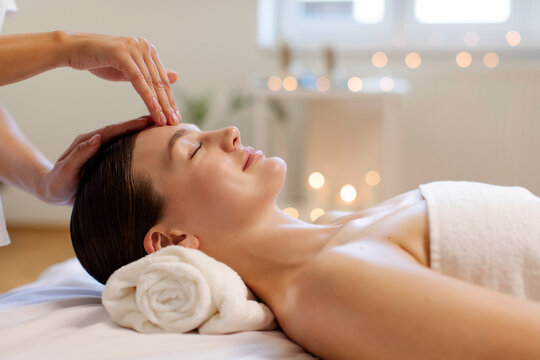 Young relaxed woman receiving head massage, enjoying beauty treatment, masseur massaging lady's forehead and face, side view - Powered by Adobe
