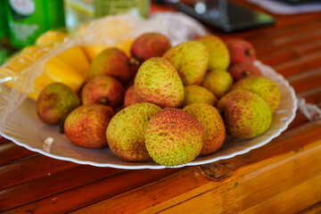 A delightful arrangement of fresh lychees and mango slices are displayed on a white plate, resting atop a warm-toned wooden surface, evoking feelings of summer abundance and healthy eating.