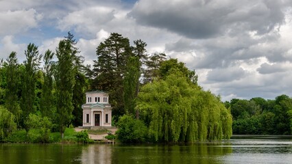 Obraz premium The lake in the spring park on a cloudy day, with green trees and an old house on the shore.