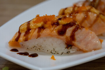 Close-up of seared salmon nigiri sushi on a white plate, topped with roe and a drizzle