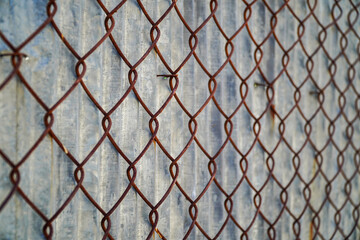 Fototapeta premium A rusty chain-link fence creates a textured and geometric pattern against a corrugated metal background. The play of light and shadow adds depth and visual interest to this abstract composition.
