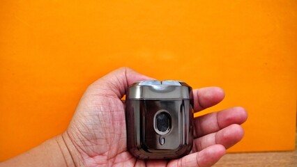Hand holding a compact electric shaver against an orange background.