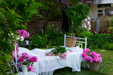 Bed with white bedding decorated with blooming pink and white peonies in a green garden