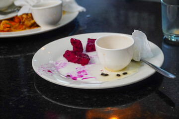 An abstract view of a half-eaten breakfast. A white plate rests on a sleek, dark surface, remnants of the meal are scattered. It showcases the aftermath, with vibrant yet messy remains.