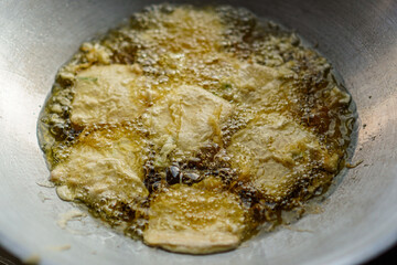 Sizzling in a pan, the culinary process unfolds as golden-brown fritters are immersed in bubbling oil, promising a delicious treat with a crispy texture and tempting aroma for food enthusiasts.