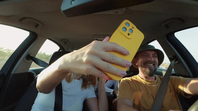 Family members capturing memorable moments using smartphone while driving during summer road trip, enjoying shared experiences and creating lasting vacation memories together