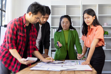Startup business team analyzing project on wooden table in modern office. Asian entrepreneurs discussing and analyzing financial data for a startup project in a modern office.