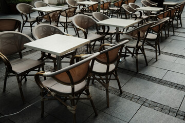 Outdoor cafe with empty wicker chairs and square tables arranged on stone pavement, urban dining concept
