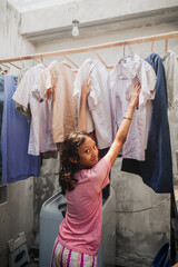 Asian teenage girl hanging wet clothes to dry while doing laundry for routine domestic chore at home looking happy smiling. Sharing household responsibilities among family members concept.
