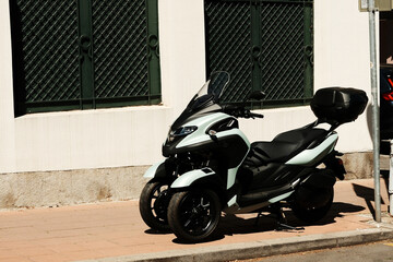Modern three-wheeled scooter with black seat parked on urban sidewalk in sunlight. Belgrade, Serbia