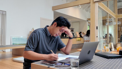 A man is sitting at a table with a laptop and a pen