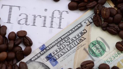 Macro close up of roasted coffee beans surround a bunch of US Dollar bills and the word Tariff. A Coffee tariff tax concept.