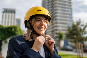 Young woman with teeth braces putting on a yellow helmet while preparing for cycling in the city