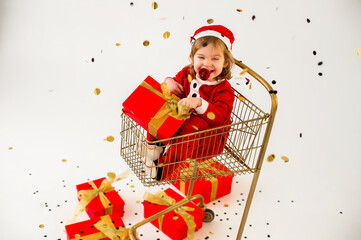 Happy toddler in Santa costume with gift box in shopping cart