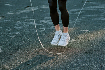 Caucasian young adult man jumping rope outdoors, lower legs and feet visible in midair, wearing athletic shoes, exercising on asphalt surface, engaging in fitness activity