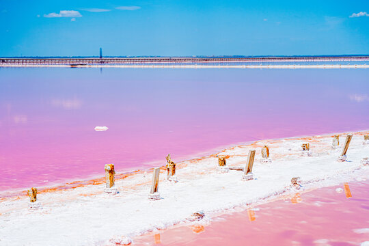 an incredibly beautiful natural phenomenon, a pink lake, a salt flat where salt is mined, with soft pink water, a blue sky, fluffy clouds and snow-white salt on the shore, and pink water in the lake w