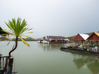 Floating raft restaurant on a reservoir with mist and drizzle in rural Thailand.