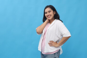 Attractive smiling young Asian woman looking at camera, empty space beside, standing pose isolated on blue background.