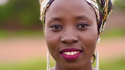 Close-up portrait of a smiling young woman wearing a patterned head wrap and dangling earrings - Powered by Adobe