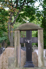 Black stone cross gravestone with crucifix, framed by a stone arch with inscription, in a cemetery.