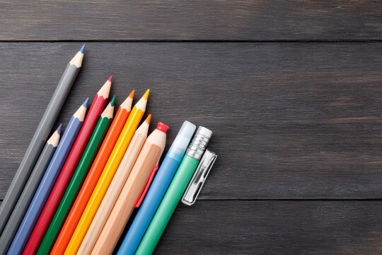 Row of pencils and pens on a wooden table.