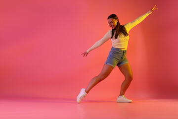 Smiling woman dancing in neon lights against pink background. Space for text