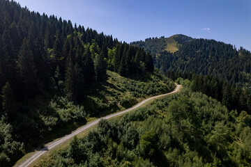 Aerial mountainous landscape with meandering path through lush green French Alps valley tourist destination winter sports near Les Gets village with rocky mountain top against a clear blue sky. 