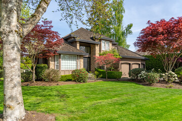 Fototapeta premium Two story stucco luxury house with nice spring blossom landscape in Vancouver, Canada, North America. Day time on May 2025.