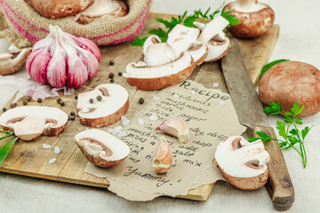 Rustic flat lay with fresh brown mushrooms, garlic, parsley, knife and handwritten recipe