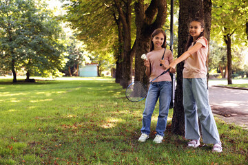 Fototapeta premium Smiling little girls with badminton rackets and shuttlecock near tree in park. Space for text