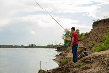 Grandfather is teaching a grandson fishing on the river beach.
