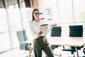 Fototapeta premium Qualified businesswoman presenting a project in a modern office workspace with professional documents and data visuals displayed
