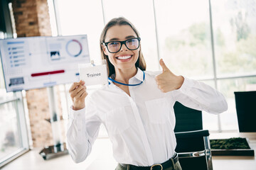 Qualified female trainee in a white shirt giving a thumbs-up gesture in a modern corporate office environment
