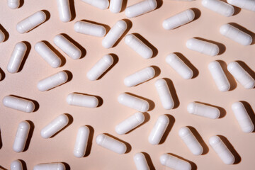 White medical capsules scattered on a pink background creating a healthcare pattern