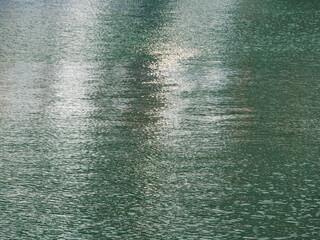 Rippling surface of a calm lake reflecting soft light and surrounding landscape during the early morning hours