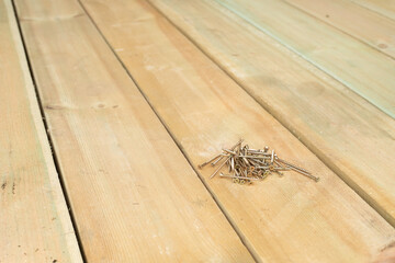 A handful of self-tapping screws are lying on a wooden board. Laying of floors. Construction works.