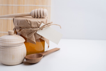 Jar of honey with wooden honey dipper on white kitchen background. Tasty honey bunker.